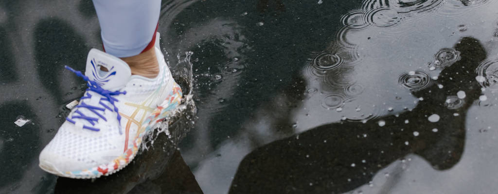 Mulher com tênis Asics branco correndo por uma poça de água